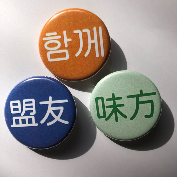 orange, purple and green pins that say ally in Chinese, Korean and Japanese